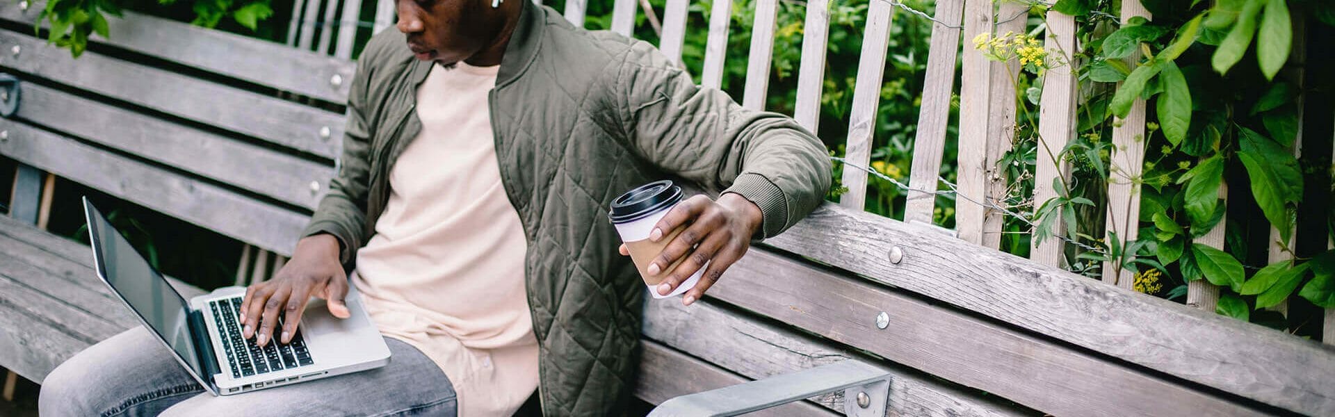 young-student-with-coffee-to-go-using-laptop-in-park-4560188